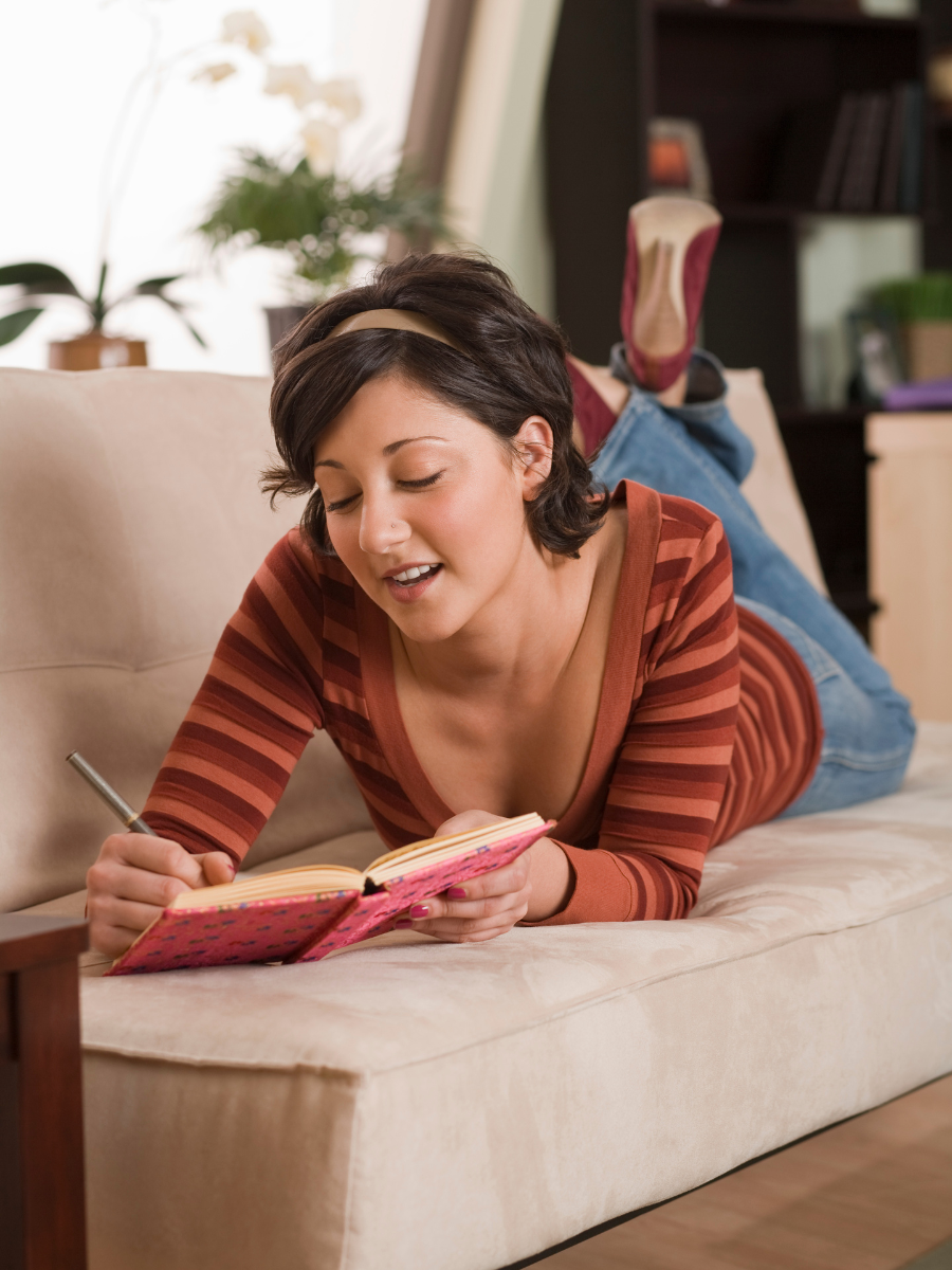 Young woman lying on couch writing in journal