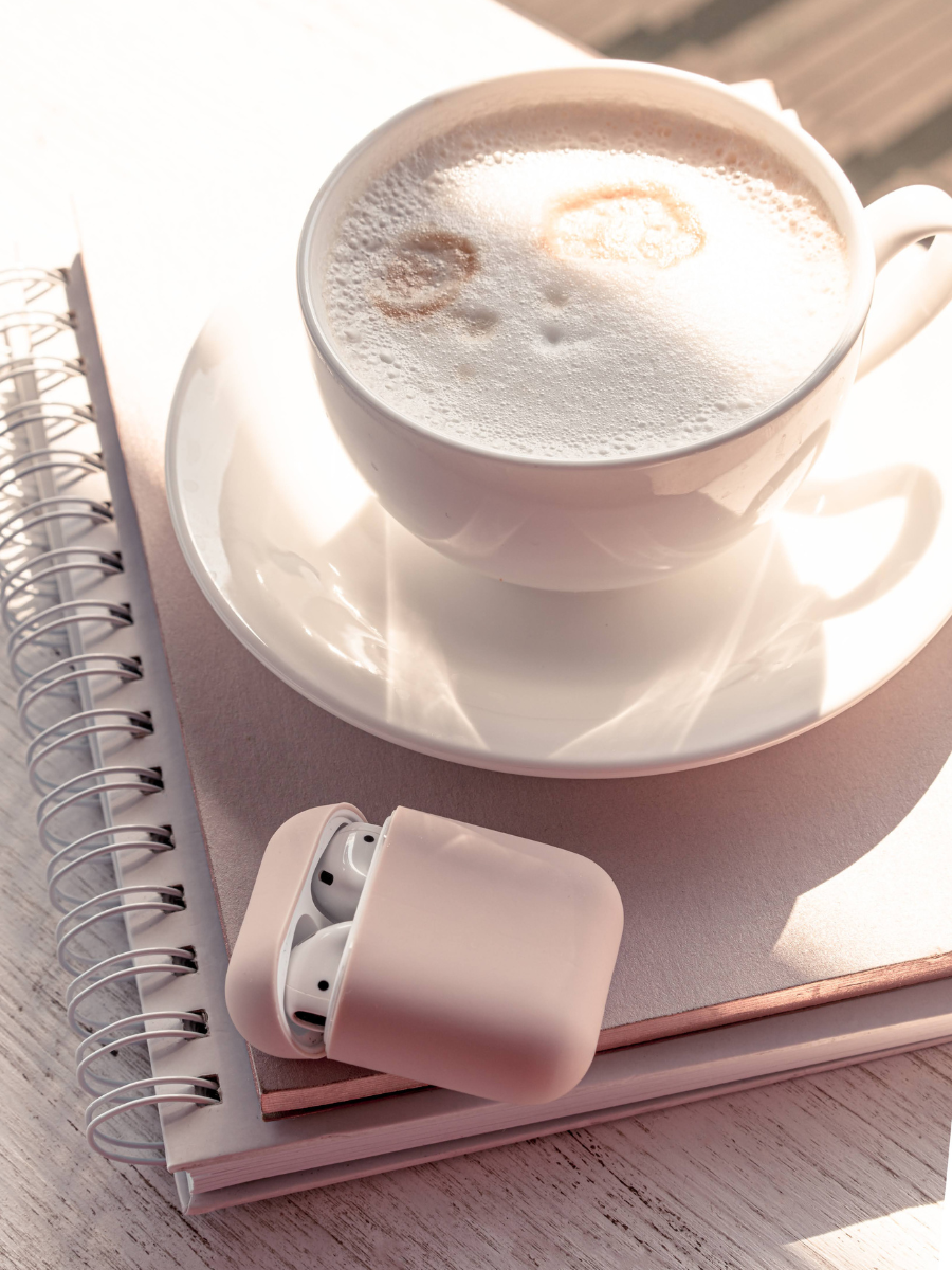 Cappuccino on top of a notebook with wireless earbuds next to it